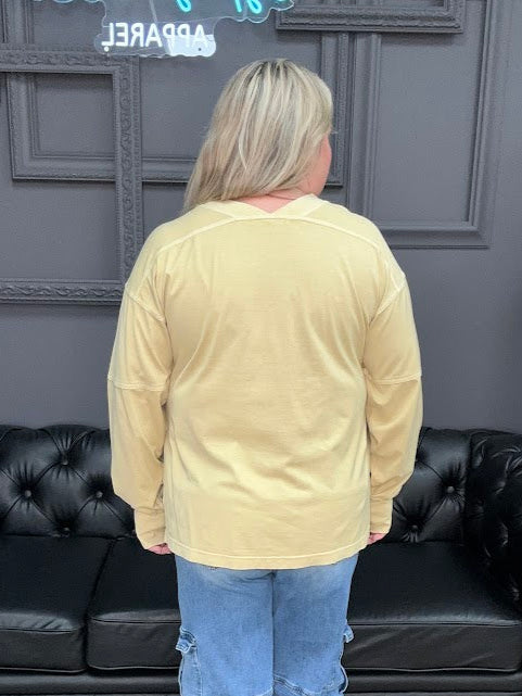 Person wearing a beige jacket and blue jeans standing in a room with black leather couches and a gray wall.