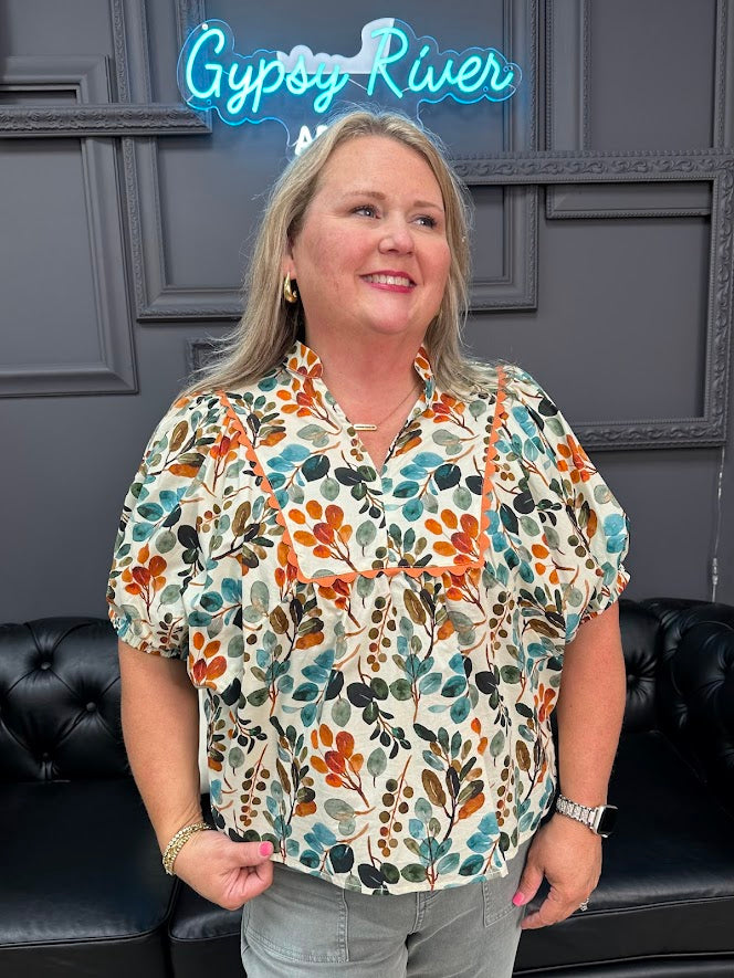 Woman wearing a patterned floral shirt standing in front of a dark wall with 'Gypsy River' neon sign.