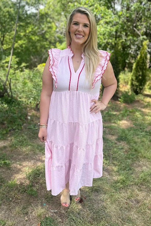 Woman in a pink dress standing outdoors with greenery in the background