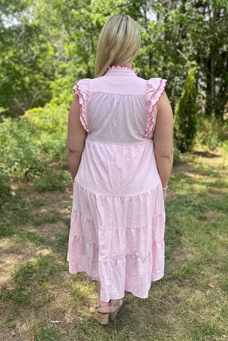 Woman wearing a pink dress standing in a grassy outdoor area with trees.