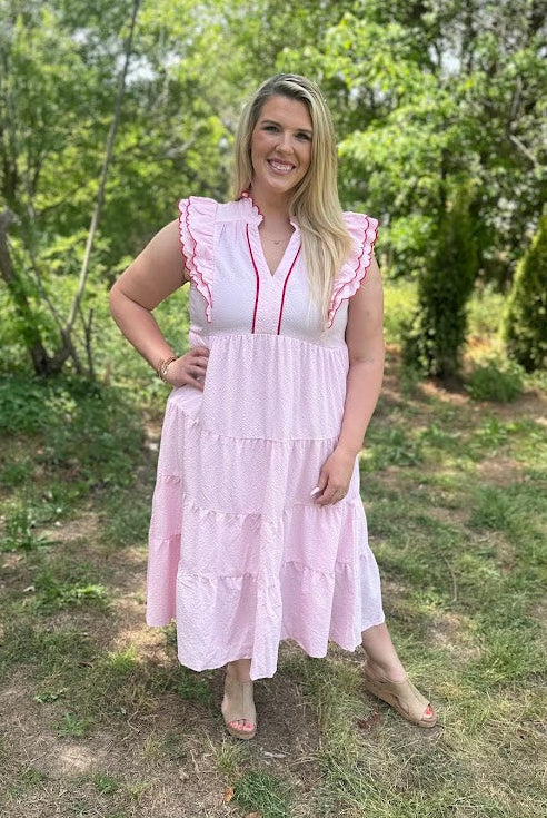Woman in a pink dress standing outdoors with greenery in the background