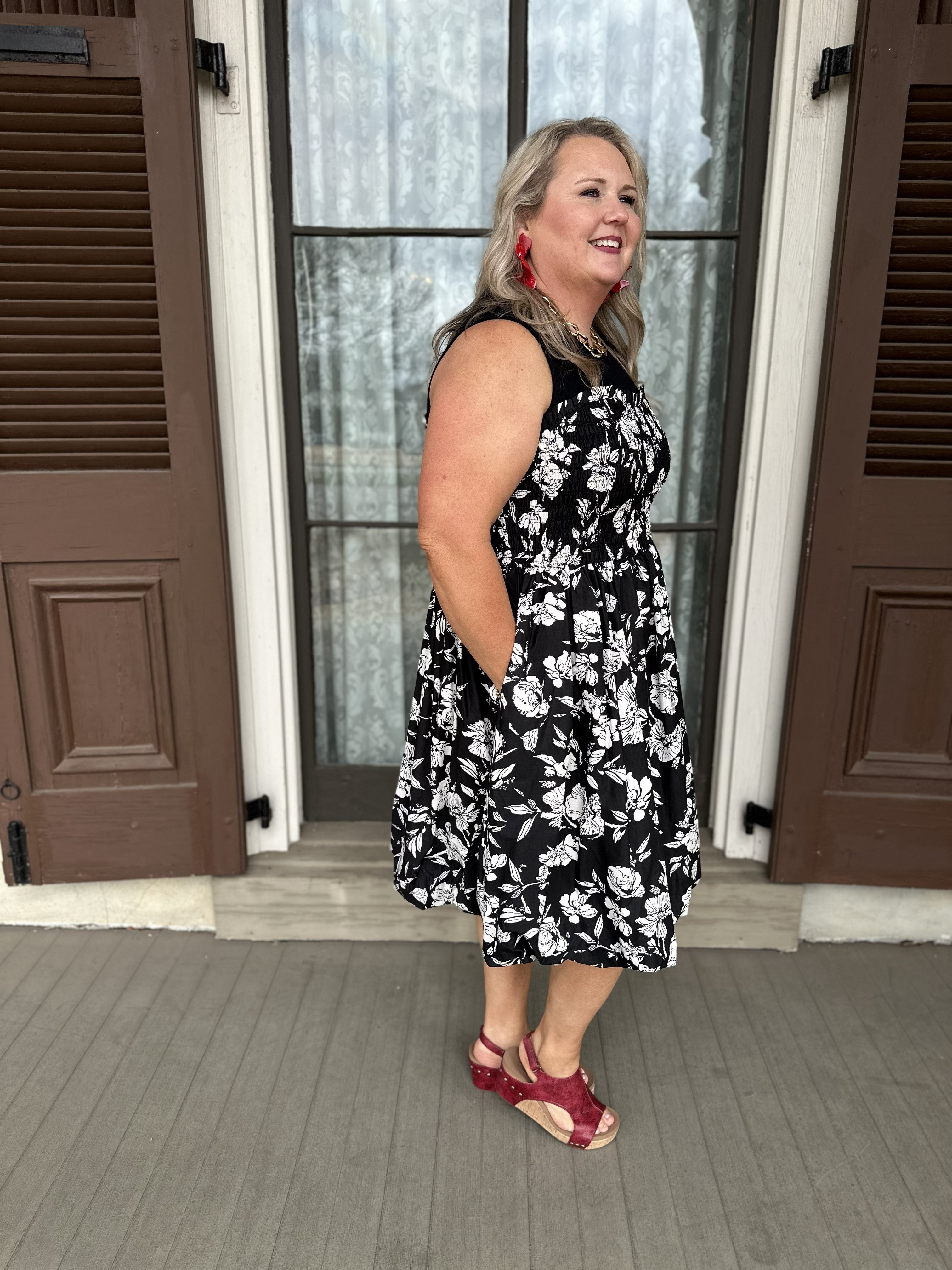 Woman wearing a black floral dress standing in front of a door.