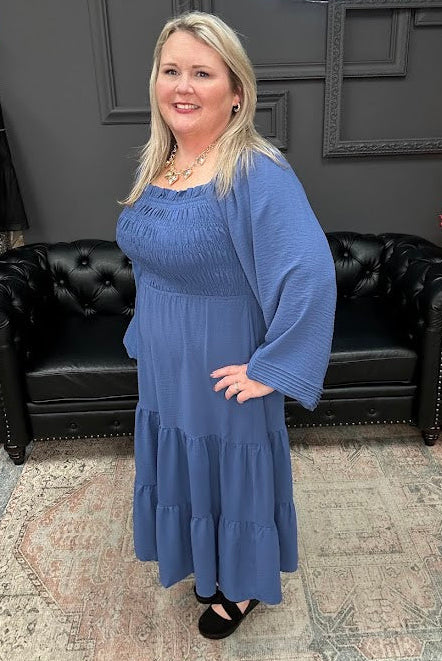 Woman in a blue dress standing in front of a Christmas tree and 'Gypsy River Apparel' sign.