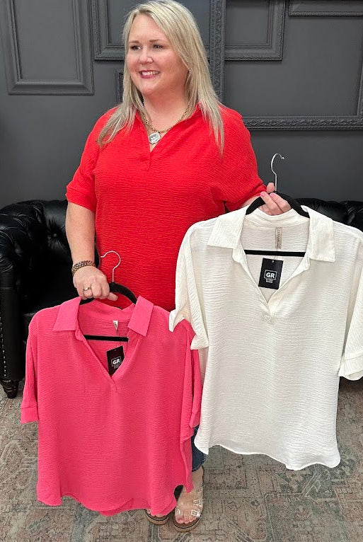 Woman holding two shirts, one pink and one white, in a store setting.