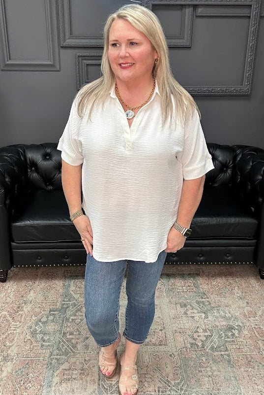 Woman in a white blouse and blue jeans standing in a room with a black leather couch and gray walls.