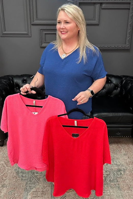 Woman holding two shirts, one pink and one red, in a store setting.