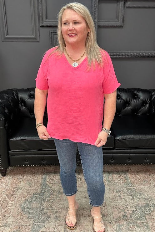 Woman in a pink shirt and jeans standing in front of a black leather couch.
