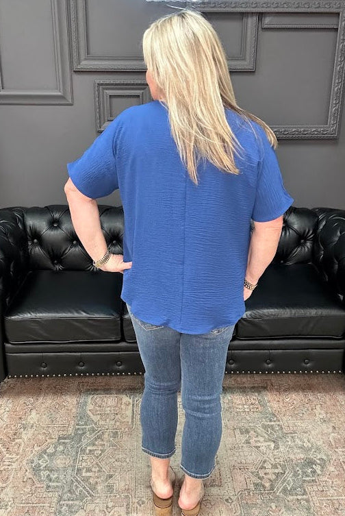 Person wearing a blue shirt and jeans standing in front of a black leather couch.