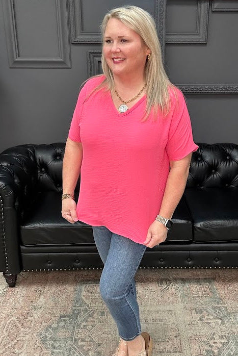 Woman in a pink shirt standing in front of a black leather couch with a gray wall and 'Apparel' sign in the background.