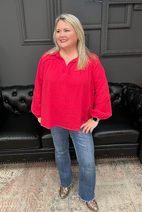 Woman in a red shirt and blue jeans standing in front of a black leather couch with 'Gypsy River Apparel' branding.