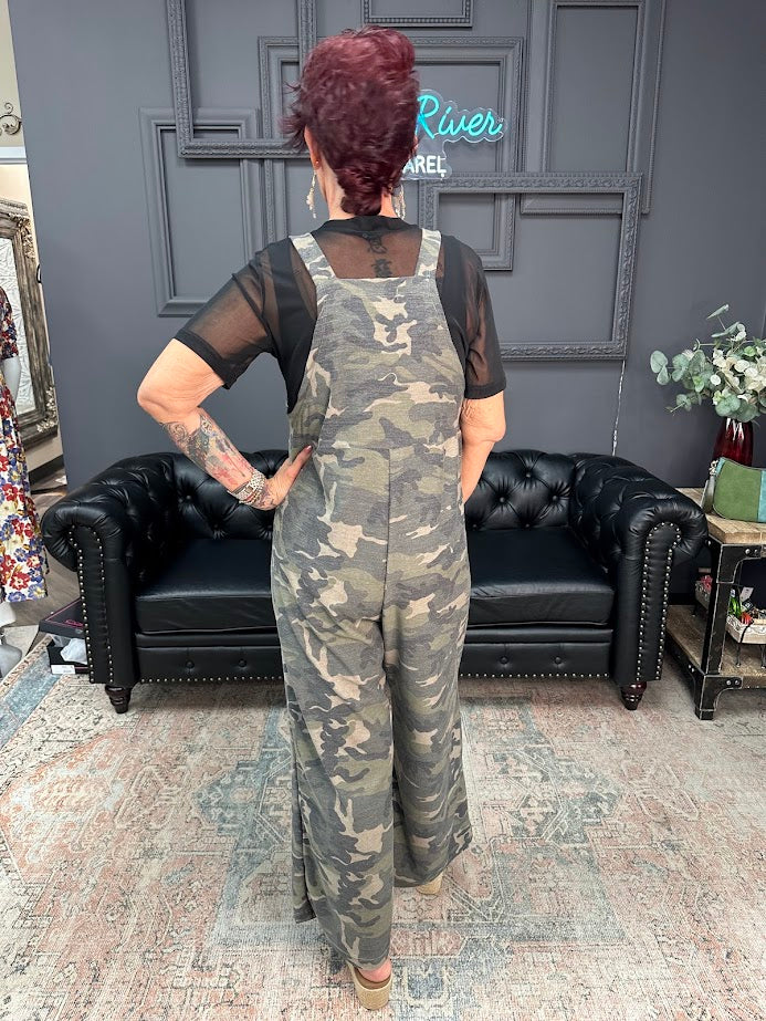 Person wearing a camouflage jumpsuit in a room with a black sofa and decorative elements.
