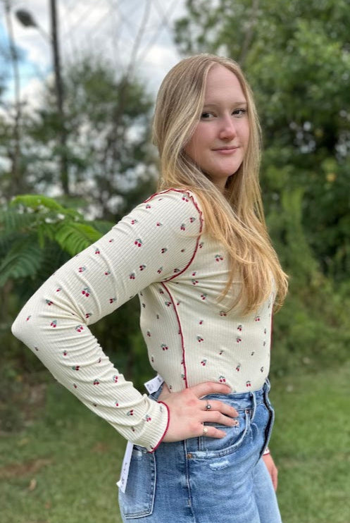 Woman wearing a cream long-sleeve top with red trim and blue jeans outdoors.