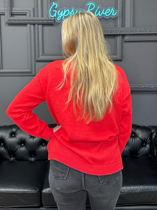 Person wearing a red sweater standing in front of a black leather couch with a gray wall featuring framed pictures and a neon sign.