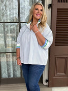 Woman standing on a porch wearing a light blue shirt and dark jeans.