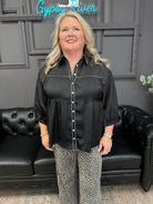 Woman wearing a black blouse and patterned pants standing in front of a black leather couch with 'Gypsy River' sign.