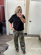 Person wearing a black polo shirt and camouflage pants taking a mirror selfie.