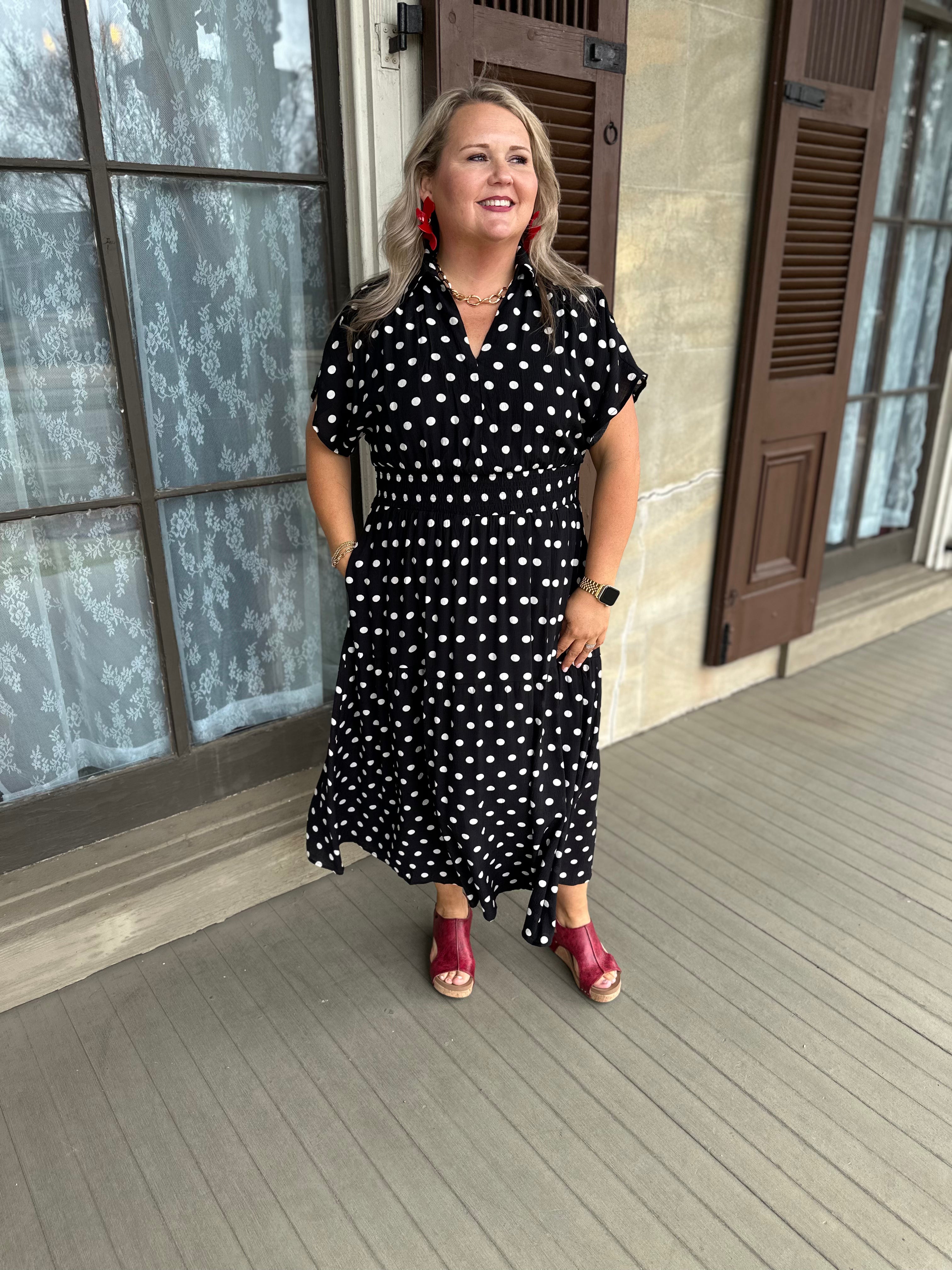 Woman in a black and white polka dot dress standing on a porch.