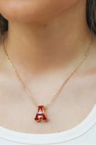 Gold necklace with a red 'A' pendant worn by a person.