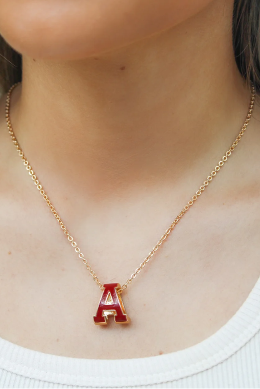 Gold necklace with a red 'A' pendant worn by a person.
