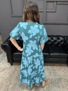 Woman wearing a green dress with blue floral pattern in a living room.