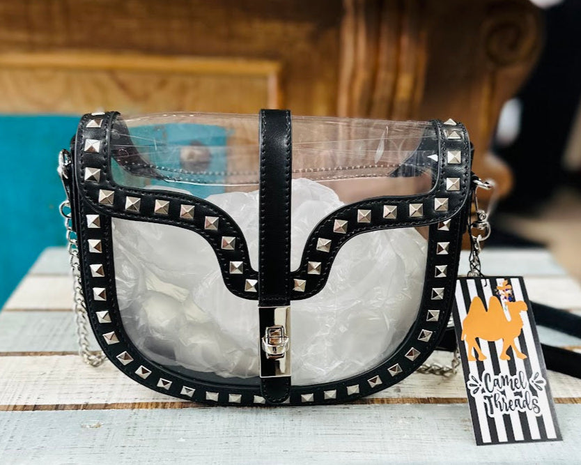 Black studded handbag with clear front section on a wooden surface, accompanied by a tag.