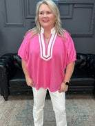 Woman wearing a pink top and white pants standing in a room with a black leather couch.