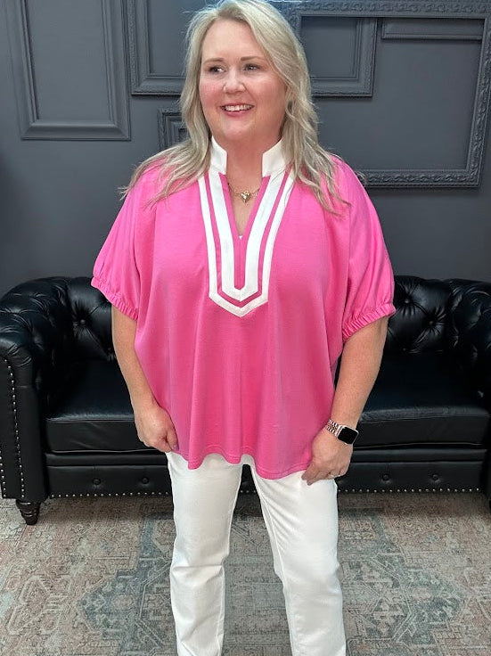Woman wearing a pink top and white pants standing in a room with a black leather couch.