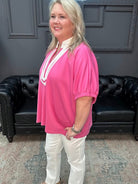 Woman wearing a pink blouse with white trim in a room with a black leather couch.