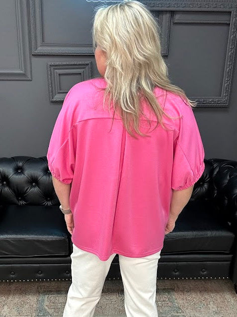 Person wearing a pink blouse and white pants standing in a room with a black leather couch.