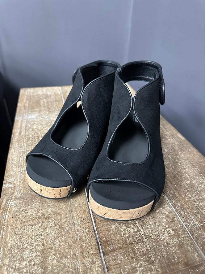 Black open-toe shoes with cork soles on a wooden surface.