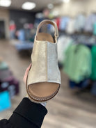 Gold glittery sandal held in front of a store with blurred background