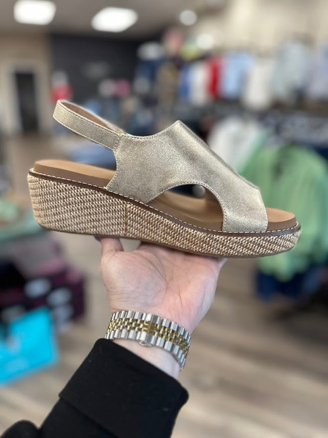 Gold wedge sandal held in a hand with a blurred store background