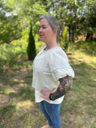 Woman wearing a white blouse and blue jeans standing outdoors with greenery in the background