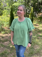 Person wearing a green shirt and blue jeans standing in a grassy outdoor area.