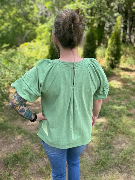 Person wearing a light green blouse with puffed sleeves in a forest setting