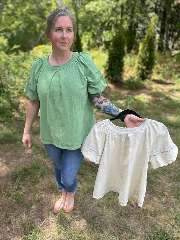 Woman holding a white blouse outdoors with greenery in the background