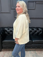 Woman in a cream blazer and blue jeans standing in a room with a black leather couch.
