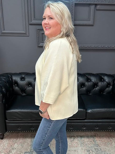 Woman in a cream blazer and blue jeans standing in a room with a black leather couch.