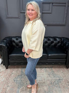 Woman in a cream blazer and blue jeans standing in a room with a black leather couch.