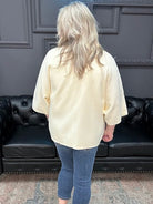 Person wearing a cream blouse and blue jeans standing in front of a black leather couch.