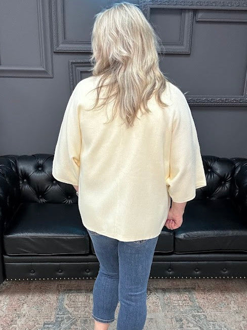Person wearing a cream blouse and blue jeans standing in front of a black leather couch.