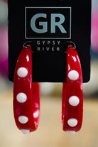 Red hoop earrings with white polka dots held by a hand against a blurred background