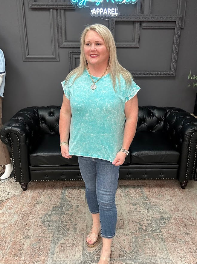 Woman wearing a light blue top and jeans standing in a room with a black leather couch and gray walls.