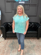 Woman wearing a light blue top and jeans standing in a room with a black leather couch and gray walls.