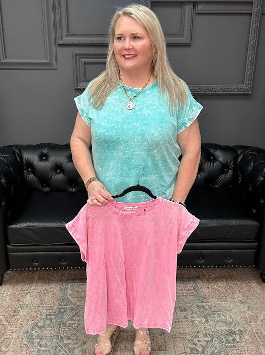 Woman holding a pink shirt in a store setting with a black leather couch and gray walls.