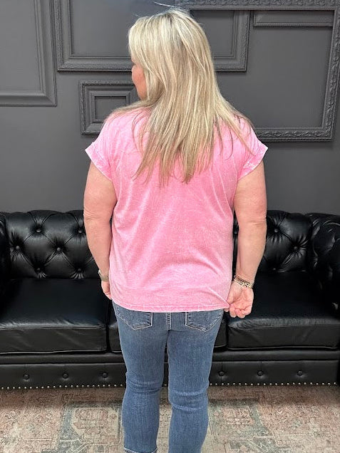 Person wearing a pink shirt and blue jeans standing in front of a black leather couch.