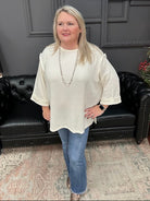 Woman wearing a white blouse and blue jeans standing in a room with a black leather couch and gray walls.