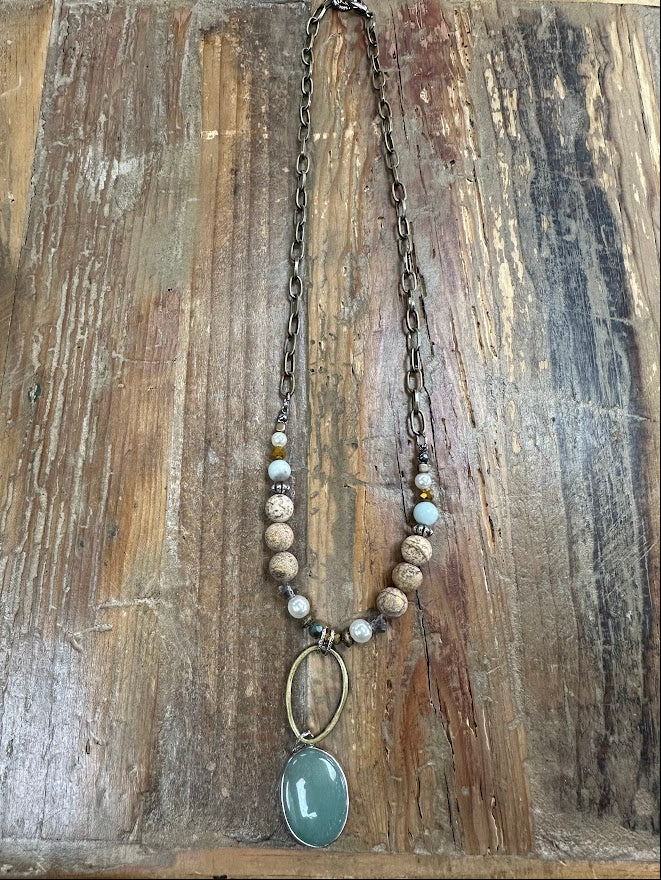 Earthy beaded necklace with sage-green oval pendant and bronze chain. Textured, neutral, and perfect for everyday styling.