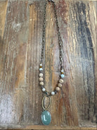 Earthy beaded necklace with sage-green oval pendant and bronze chain. Textured, neutral, and perfect for everyday styling.