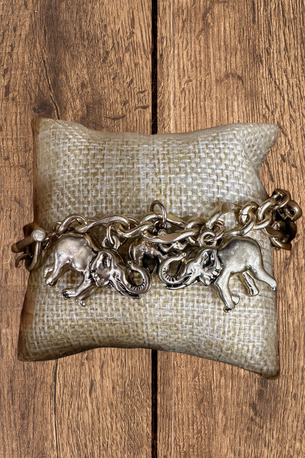 Bracelet with elephant charms on a textured pillow against a wooden background